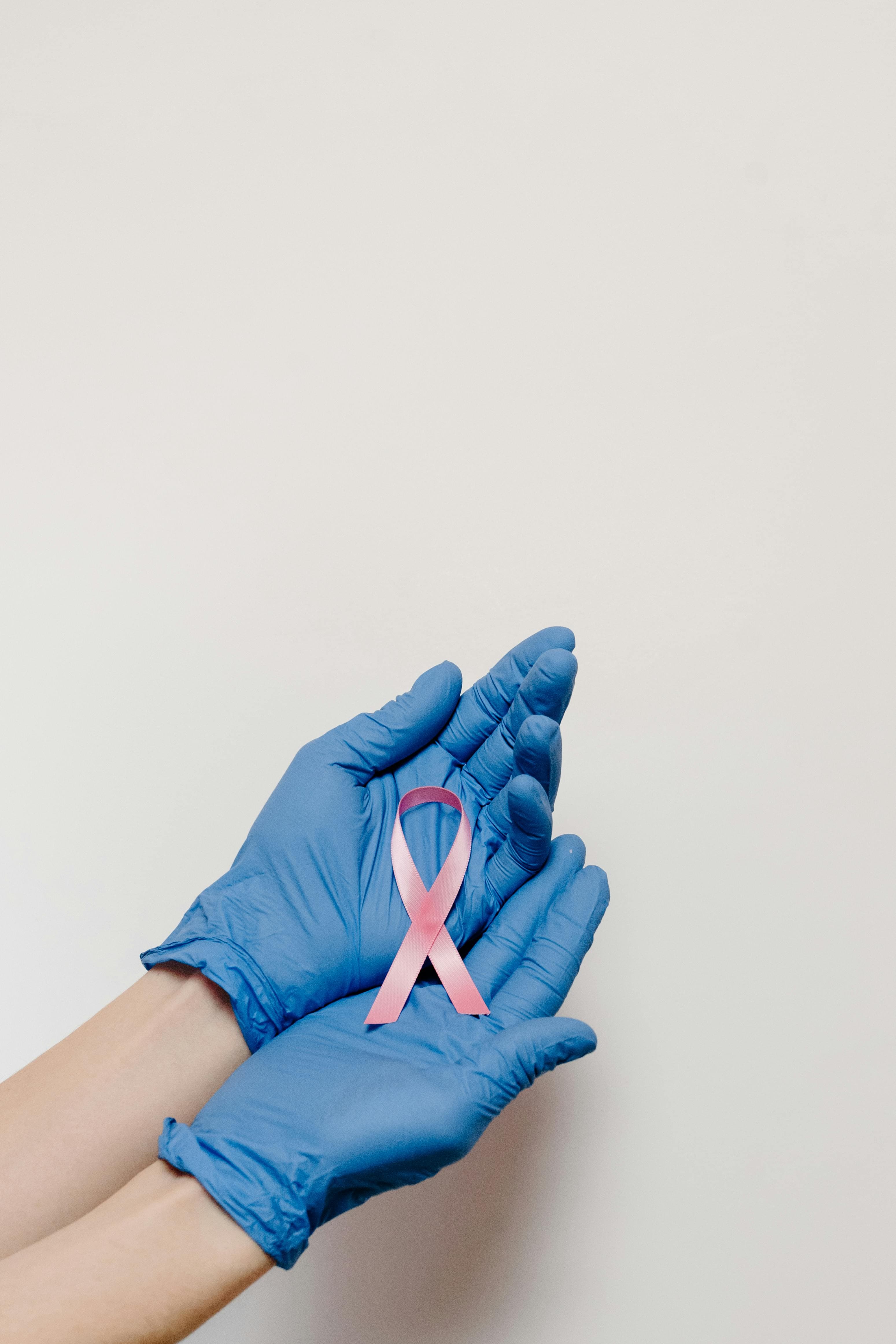 Blue-gloved hands holding a pink ribbon for cancer awareness.