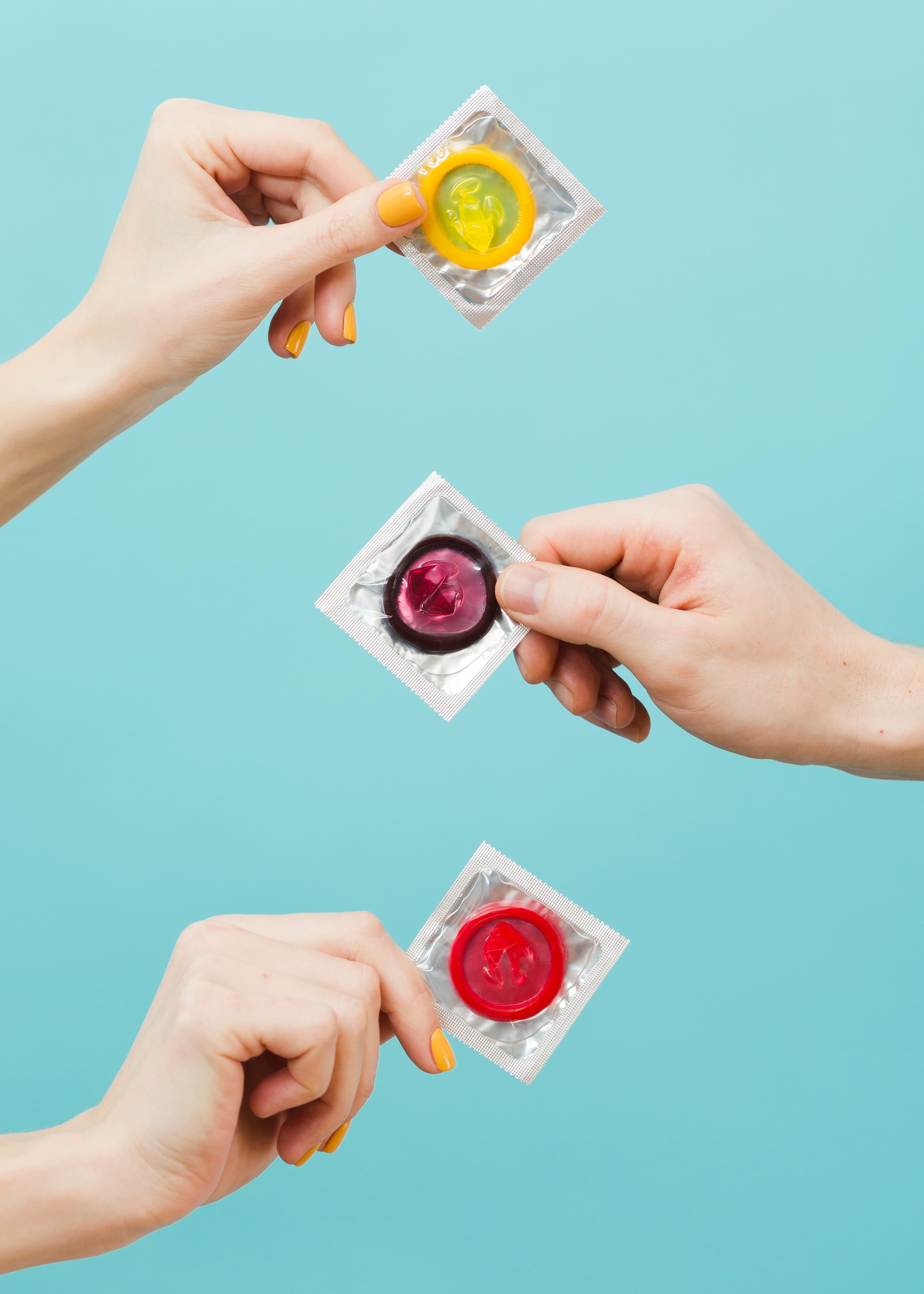 Hands holding colorful condom packets against a blue background.