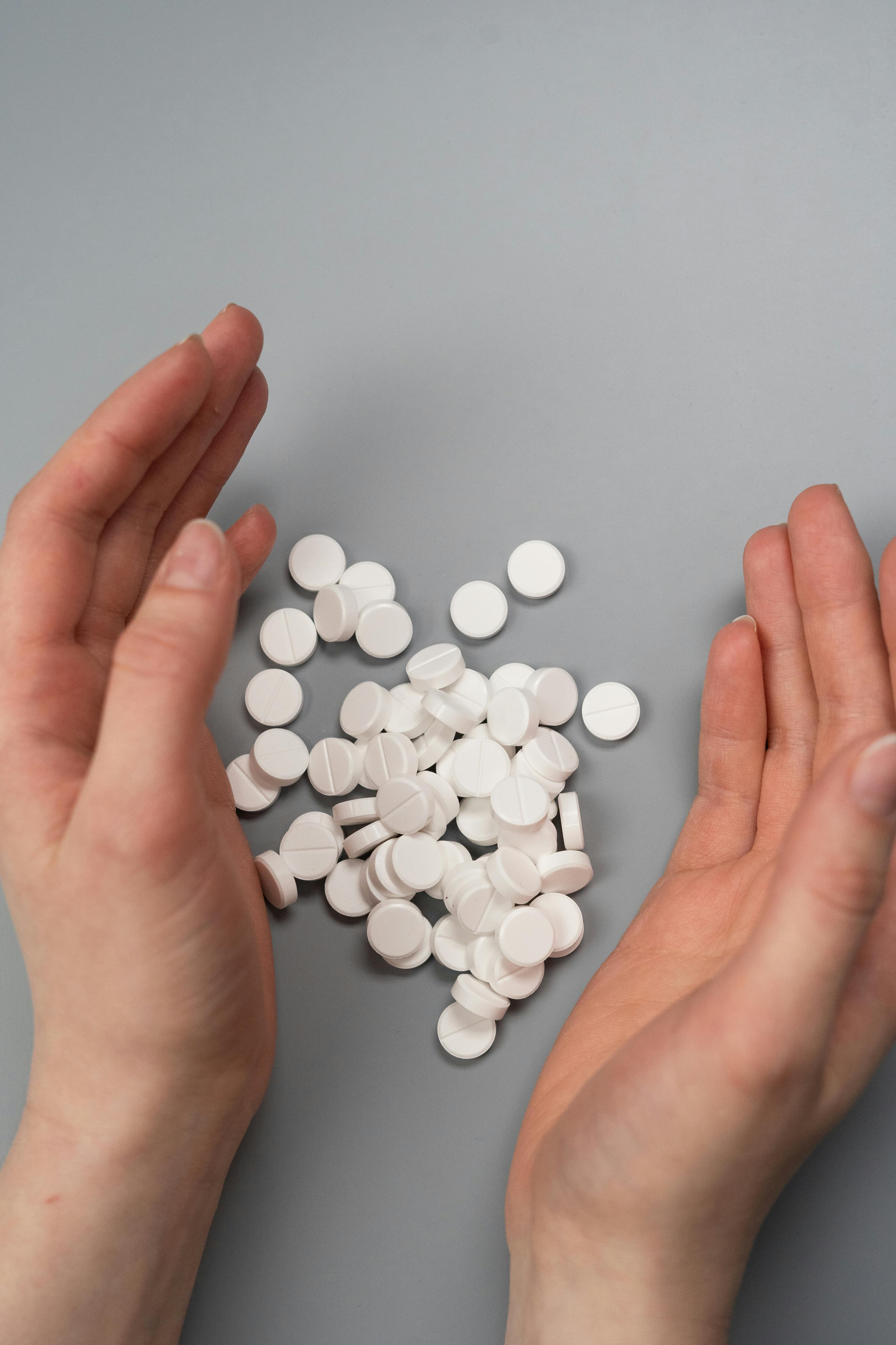 Hands surrounding a group of contraception pills on a gray surface.